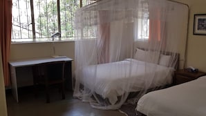 Un dormitorio con una cama bajo una mosquitera, un escritorio y una mesita de noche con lámpara.