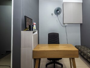 Una habitación pequeña con una mesa de madera, una silla de oficina negra, una cama con ropa de cama de estampado de cebra, un armario blanco y un ventilador de pared.