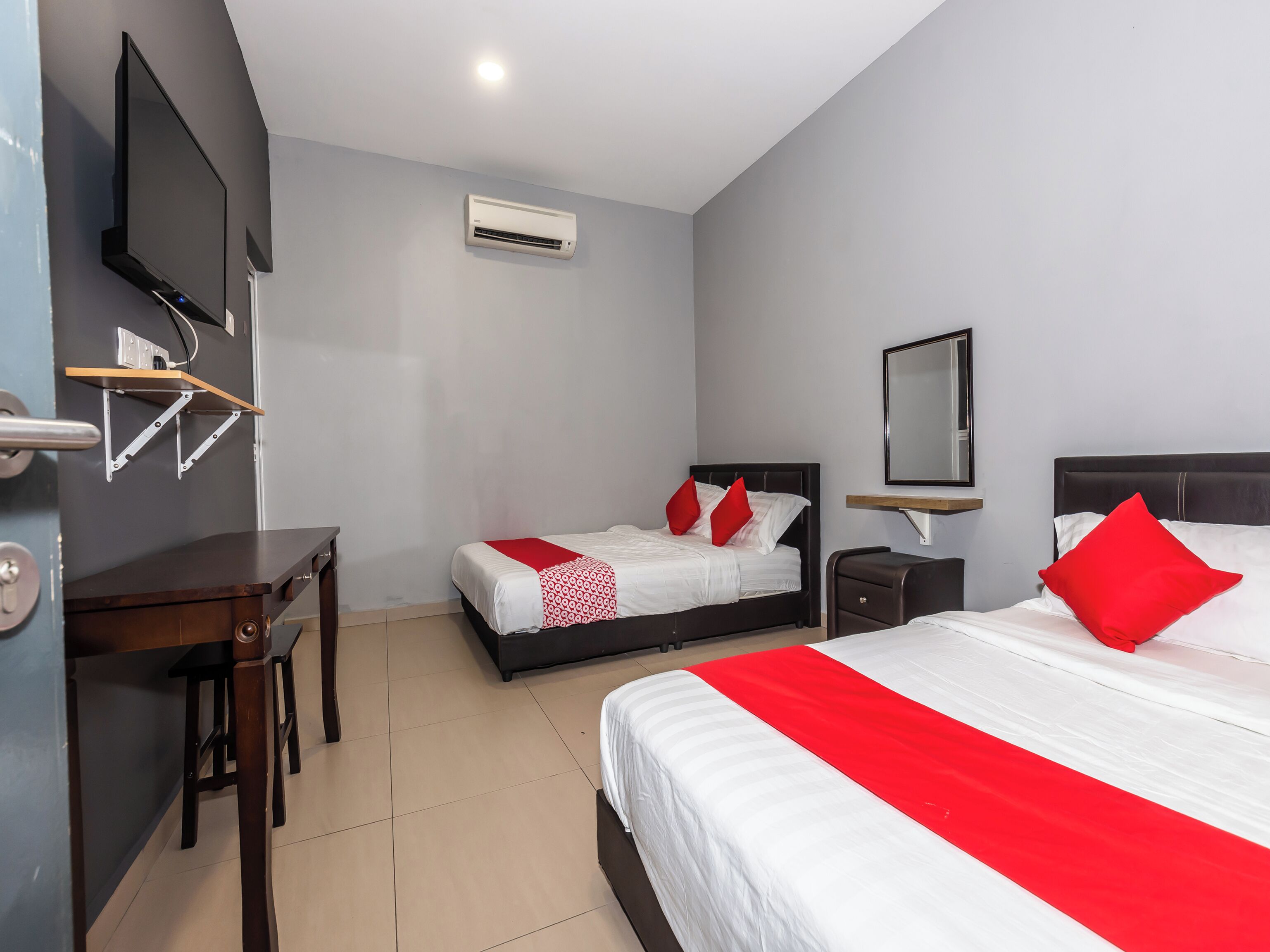 A hotel room with two beds, a desk, a chair, a TV, and an air conditioning unit.