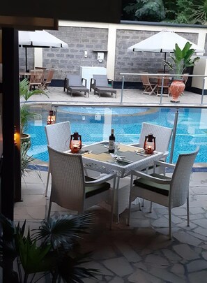 A poolside area with a table and chairs, a pool, and umbrellas.