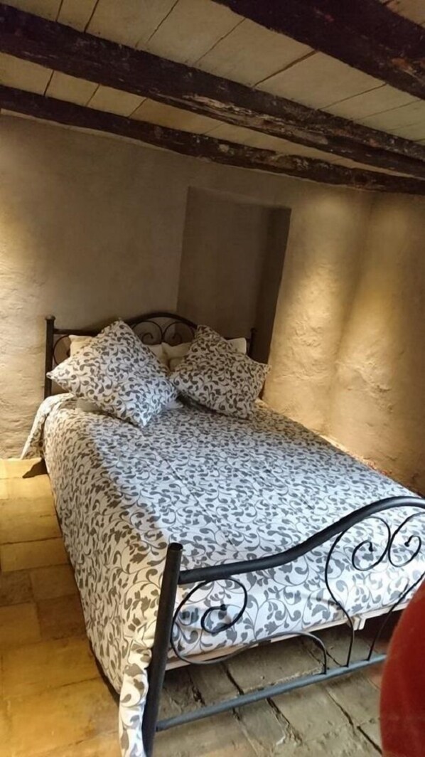 Ein kleines Zimmer mit einem Einzelbett, einer gemusterten Bettdecke und passenden Kissen. Das Bett steht an einer Wand mit strukturierter Oberfläche, und das Zimmer hat ein schlichtes, zweckmäßiges Design.