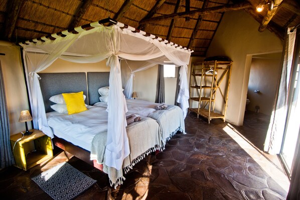 A four-poster bed with a canopy, a bedside table with a lamp, and a patterned rug. - Palmwag Lodge (Palmwag)