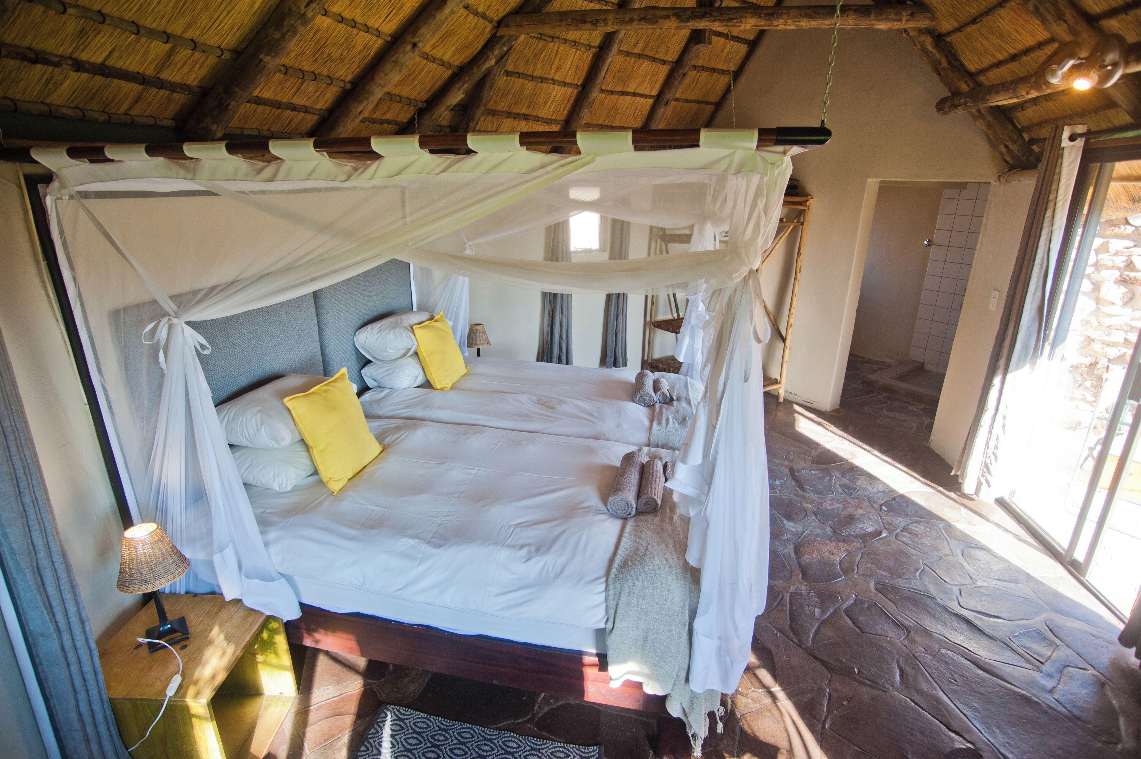 A bed with a canopy, a bedside lamp, and a stone floor.