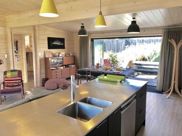 A modern kitchen with a central island, stainless steel appliances, and pendant lighting. - Modern Kowhai Cottage (Wanaka)