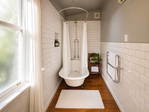 A bathroom with a freestanding bathtub, a shower curtain, a wooden shelf with towels, and a window. - Crescent Villa - Palm Beach Views and Spa (Palm Beach)