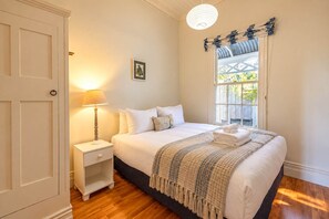 A bedroom with a bed, bedside table, lamp, and a window with curtains. - Crescent Villa - Palm Beach Views & Hot Tub (Palm Beach)