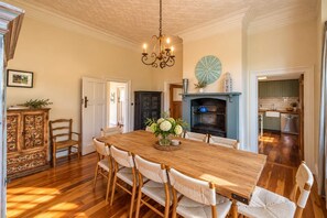 A dining room with a wooden table, six chairs, a chandelier, a fireplace, and a kitchen in the background. - Crescent Villa - Palm Beach Views & Hot Tub (Palm Beach)