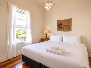 A hotel room with a bed, a nightstand, a lamp, a star-shaped hanging light, a window with curtains, and a wall with a text poster.