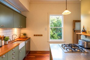 A kitchen with wooden cabinets, a window, a gas stove, and a hanging light fixture. - Crescent Villa - Palm Beach Views & Hot Tub (Palm Beach)