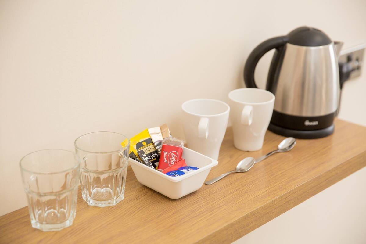 A wooden shelf with a kettle, two glasses, a bowl of snacks, and a spoon.