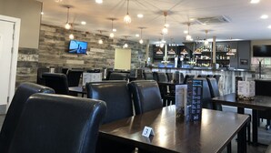 A restaurant interior with multiple tables and chairs, a bar area, and a television mounted on the wall. - Halfway Hotel (Coalville)