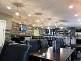 A restaurant interior with multiple tables and chairs, a bar area, and a television mounted on the wall.