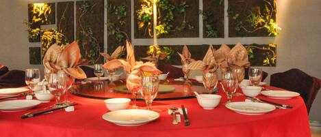 A dining table set for a meal with a red tablecloth, surrounded by chairs, and a wall with vertical panels.