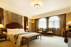 A hotel room with a large bed, a desk, two chairs, a small table, and a lamp. - Grand Palace Hotel (Guangzhou)