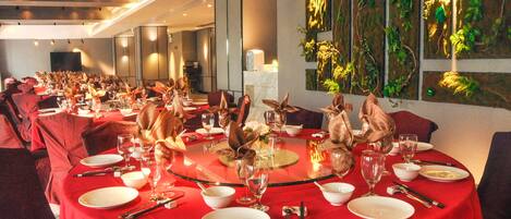 A dining area with round tables set for a meal, featuring red tablecloths and elegant table settings.