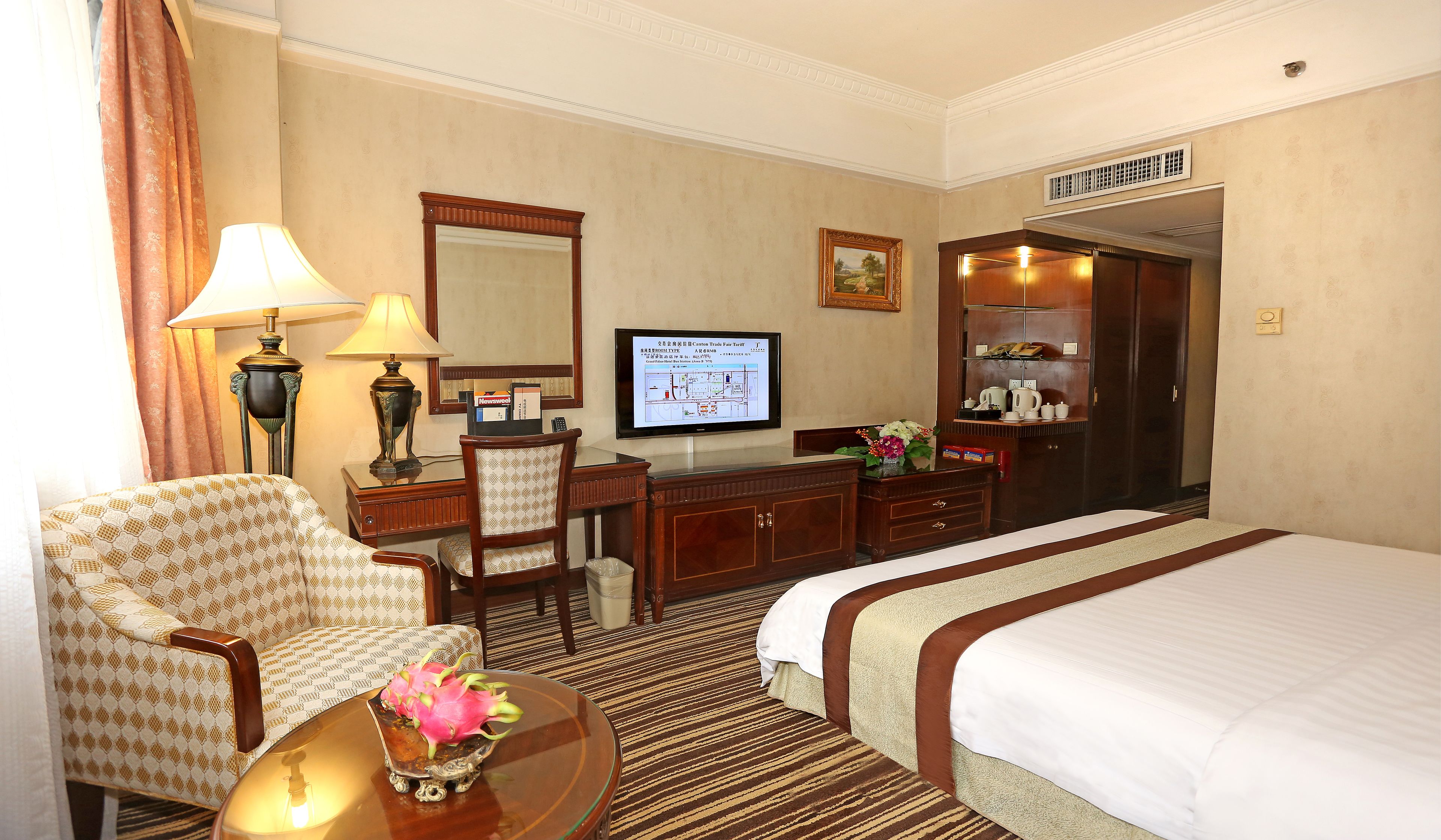 Habitación de hotel con cama, escritorio con lámpara, silla, televisor y cómoda.
