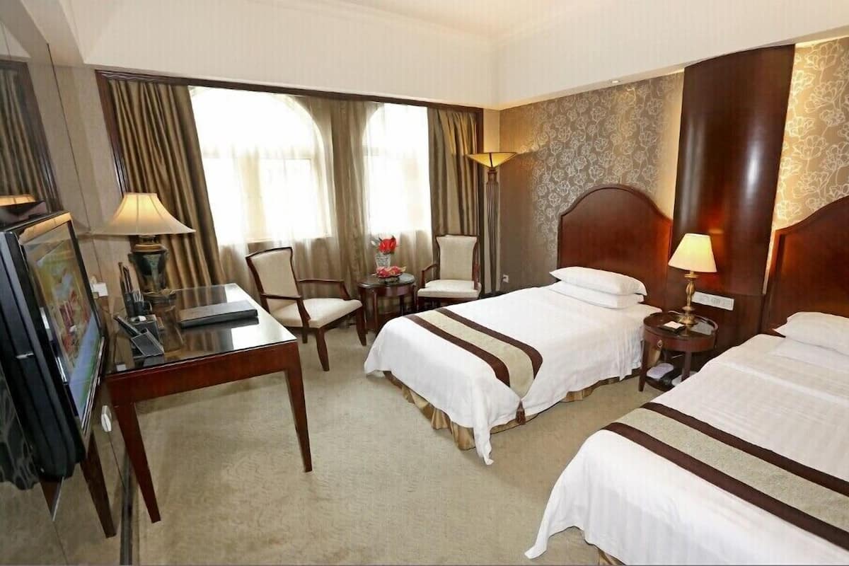 A hotel room with two beds, a desk, a chair, and a lamp.