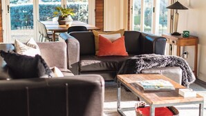 Un salon chaleureux avec un canapé en cuir, une table basse en bois et une vue sur un jardin grâce à de grandes fenêtres.