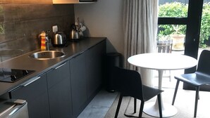 A modern kitchen with a built-in microwave, stainless steel sink, and a kettle on the counter. There is a round table with two chairs in front of a large window with curtains.