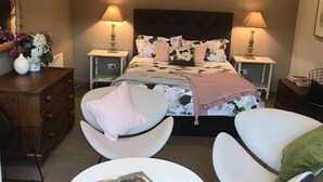 A bedroom with a large bed, two bedside tables with lamps, a dresser, two chairs, and a small round table with a pinecone centerpiece.