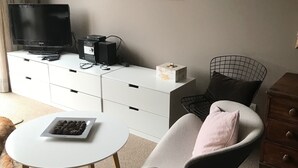 A living room with a television, a white cabinet, a small table with a bowl of fruit, and a pet dog.