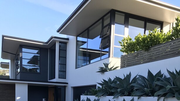 A modern two-story house with large windows, a flat roof, and a white exterior wall with a vertical garden.
