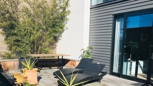 A wooden deck with potted plants, outdoor furniture, and a modern building in the background.