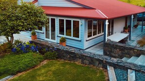 A house with a red roof, stone steps, and a garden with blue flowers. - Maison du Campagne in French Farm, Akaroa (Wainui (Banks Peninsula))