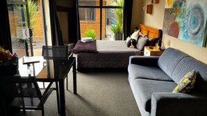 A modern hotel room with a bed, a sofa, a dining table, and a large window offering a view of the outside. - Free Wifi/Breakfast,clean,private studio Greymouth (Greymouth)