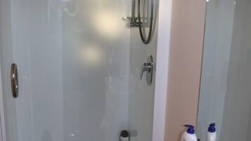 A glass-enclosed shower with a handheld showerhead and a wall-mounted faucet. There are two bottles of Dove body wash on the counter.