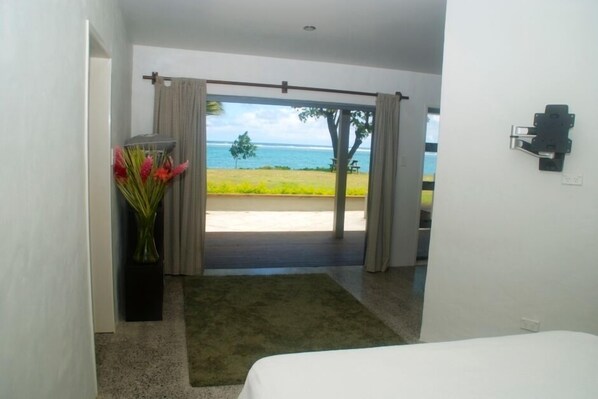 A hotel room with a bed, a view of the beach, and a vase of flowers. - Beach Haven, right on the beach (Vaimaanga)
