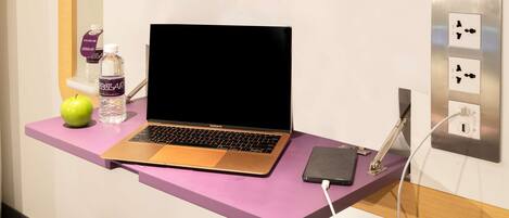 A MacBook Air on a purple desk with a water bottle, an apple, and a phone charger.