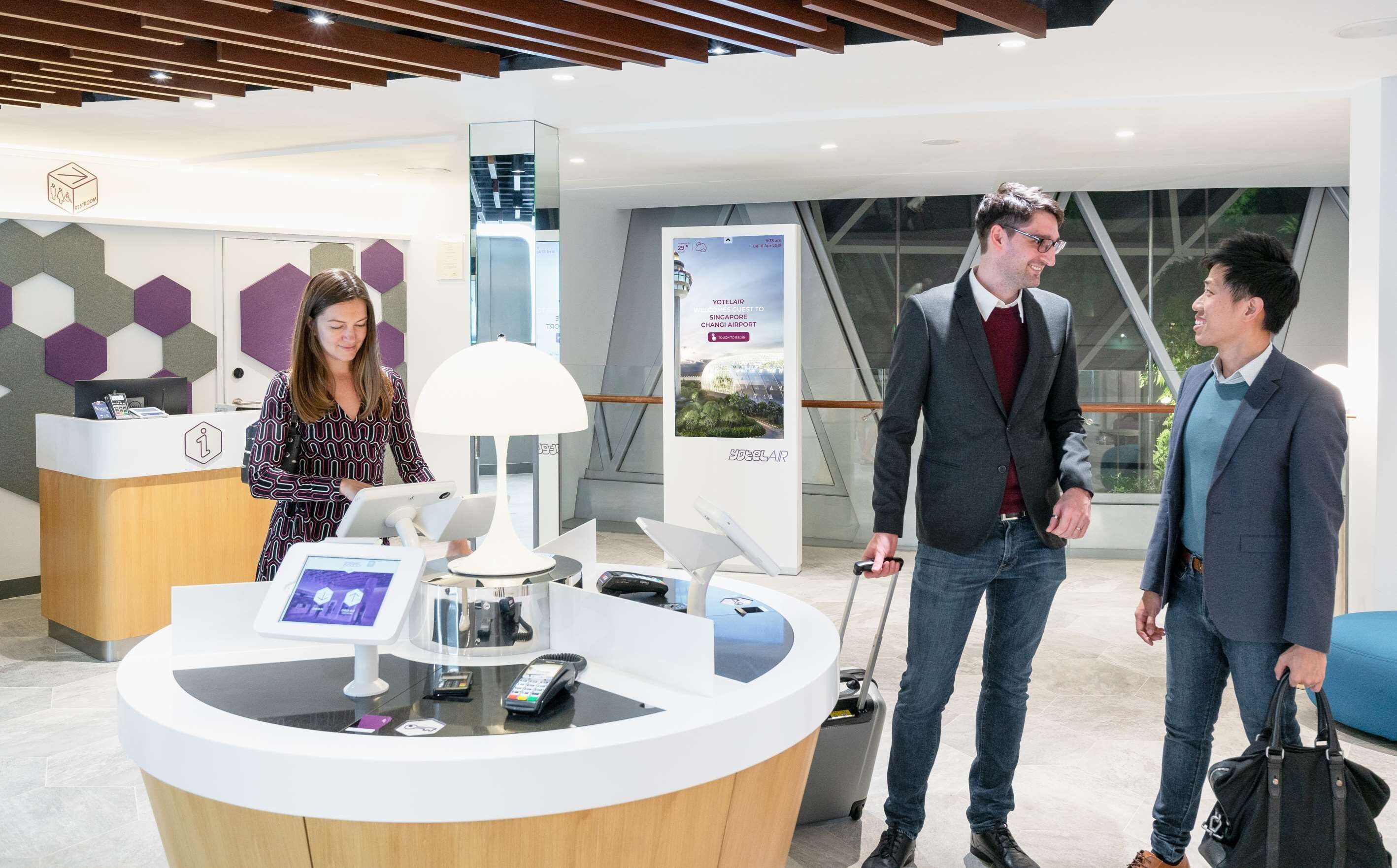 Un espace d’accueil comprenant un comptoir, un écran numérique et une affiche faisant la promotion des services de Yotelair.