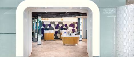 A modern hotel lobby with a reception desk, a waiting area, and a geometric patterned wall.