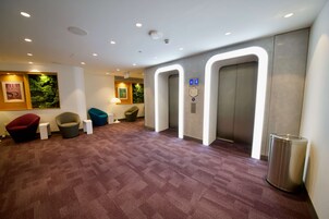 Un vestíbulo moderno con piso alfombrado, un mostrador de recepción y dos ascensores.