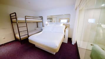 Une chambre d’hôtel avec un lit superposé, un lit simple, une table de chevet avec une lampe, un miroir et une cabine de douche en verre.