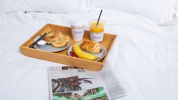En bakke med morgenmad på sengen, inklusiv avis, kop og juice.