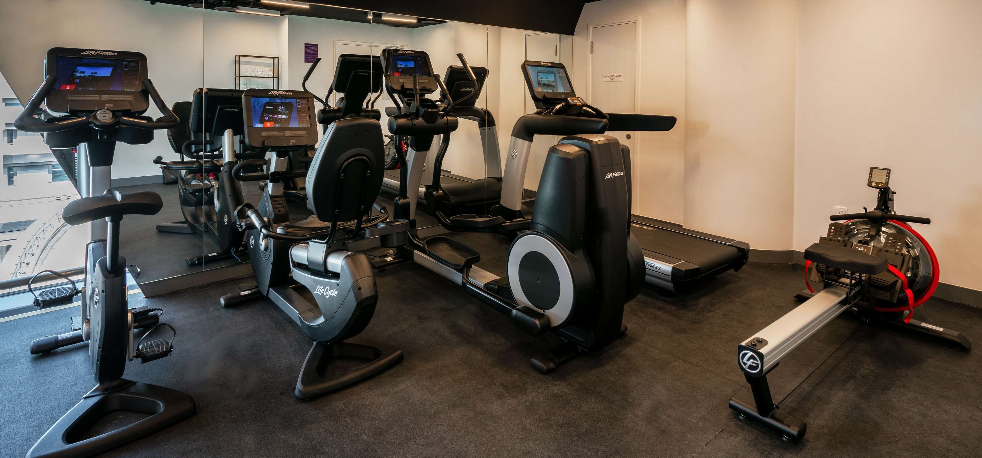Et fitnesscenter med forskellig træningsudstyr, herunder løbebånd, crosstrainer og romaskine.