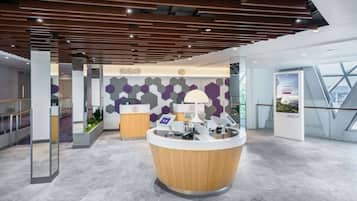 A modern reception area with a wooden reception desk, a digital information kiosk, and a geometric patterned wall.
