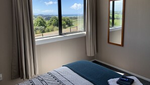 A bedroom with a large window offering a scenic view of green fields and hills.
