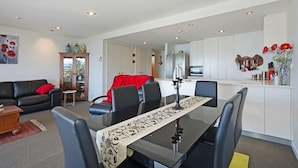 A modern living room with a dining area, a kitchen, and a hallway. - Waterfront Escape - Nelson Waterfront Apartment (Nelson City)