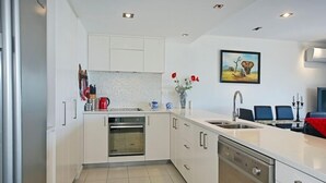 A modern kitchen with white cabinetry, a built-in oven, a dishwasher, and a large island with a sink. - Waterfront Escape - Nelson Waterfront Apartment (Nelson City)