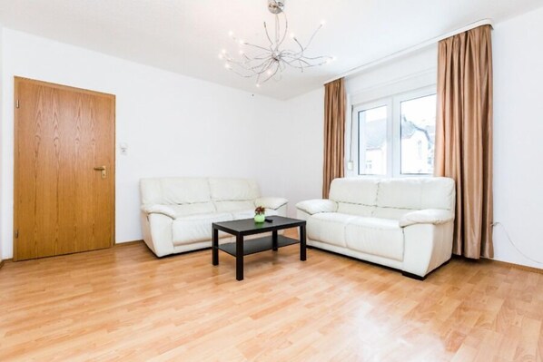 A living room with two white sofas, a wooden coffee table, and a wooden floor. - Apartments Overath Immekeppel (Overath)