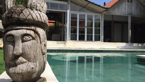 A stone sculpture in a pool area with a house in the background. - Villa Balimasan (Kerobokan)