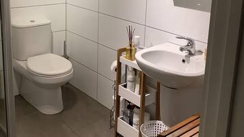 A small, modern bathroom with white tiles, a toilet, a sink, and a mirror.