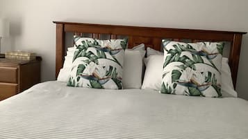 A neatly made bed with striped bedding and two pillows with a tropical leaf pattern.