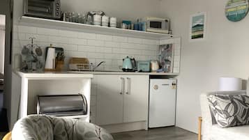 A compact kitchenette with a microwave, toaster, and coffee maker on the countertop, a small refrigerator, and a sink.