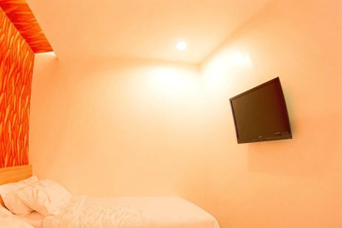 A bedroom with a bed, a wall-mounted TV, and a ceiling light.