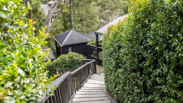 A wooden staircase leading to a building with a dark roof, surrounded by lush greenery.