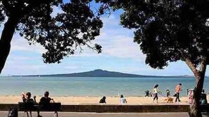 A beach scene with people walking and sitting on a bench, overlooking the sea.